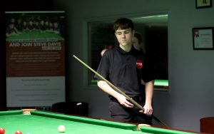 Oliver Sykes in a black EPSB polo shirt prepares to play a shot.